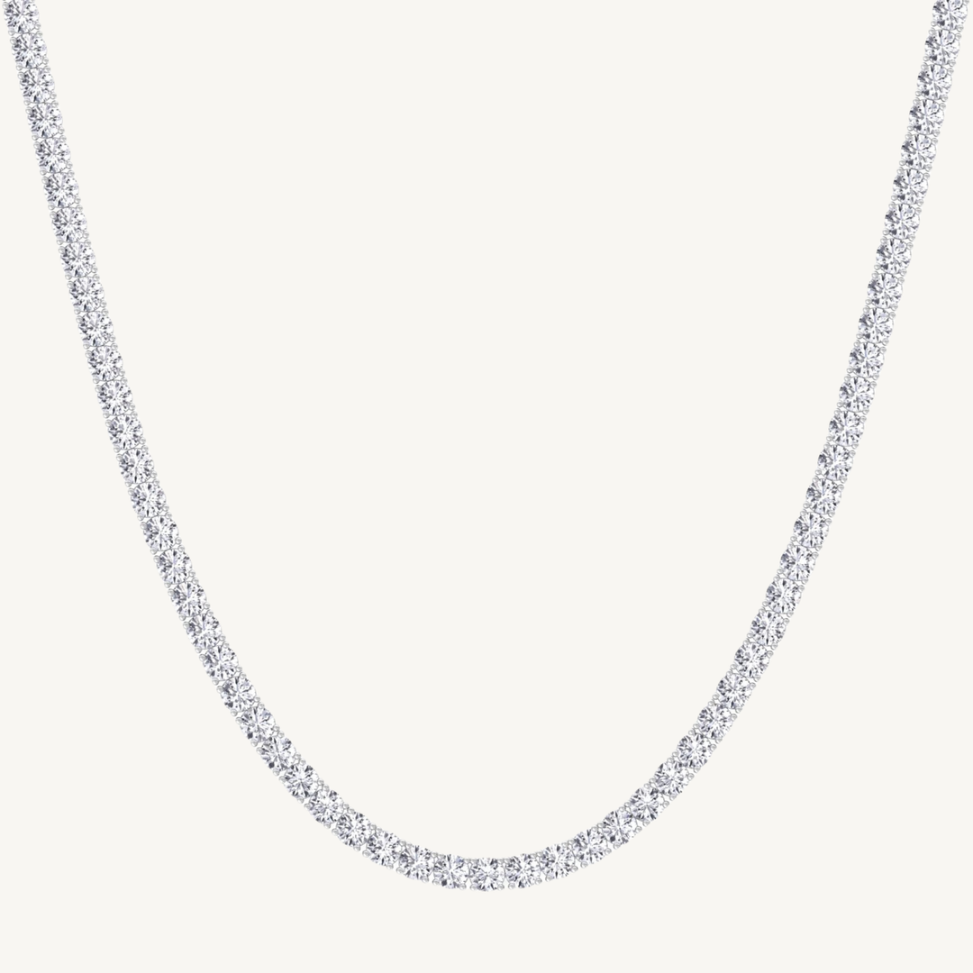 A white gold-toned tennis chain necklace paved with small clear stones, shown against a plain off-white background.