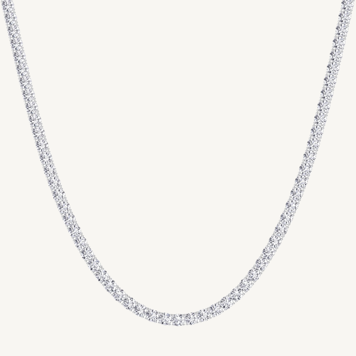 A white gold-toned tennis chain necklace paved with small clear stones, shown against a plain off-white background.