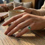 Hand with a green gemstone ring on a wooden table with a cup in the background